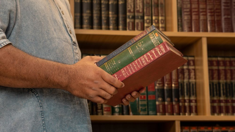 طالب يحمل كتباً عربية في مكتبة جامعية لكلية الإلهيات
